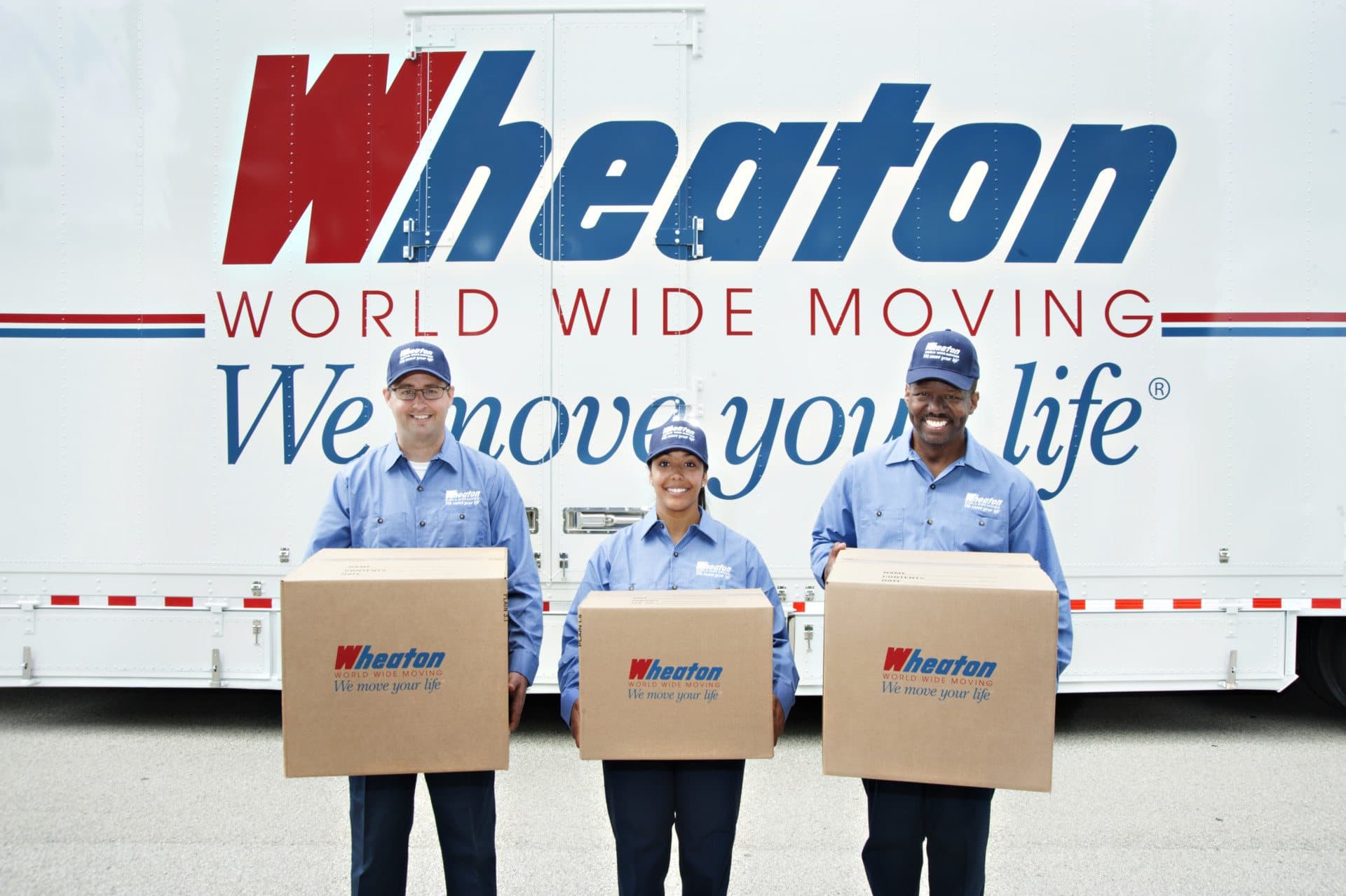 Three Delaware Moving and Storage professionals holding packed boxes in front of a branded Wheaton World Wide Moving truck